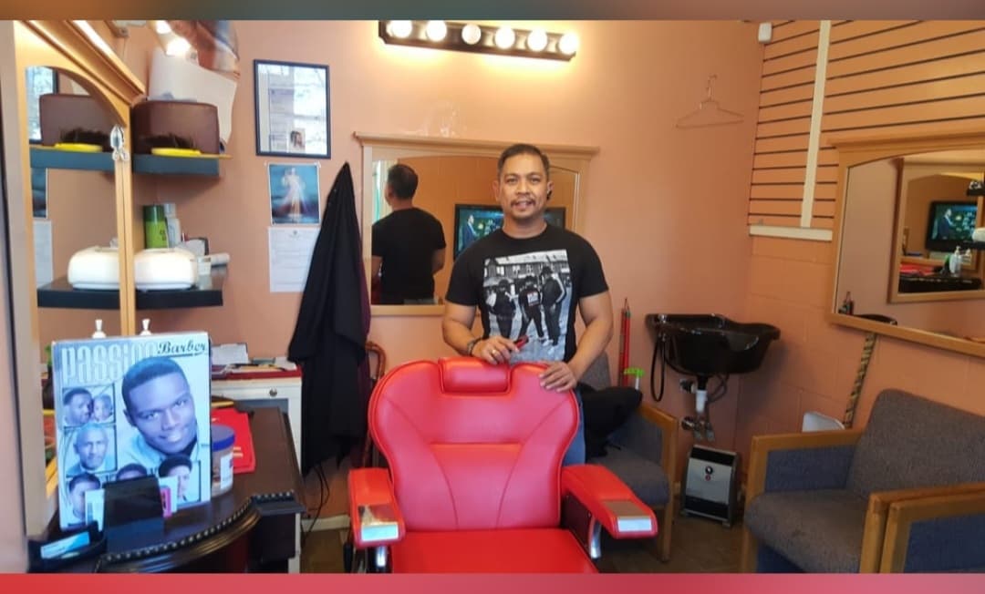 One of the barbers at Gloria Hair Salon standing beside a red barber chair